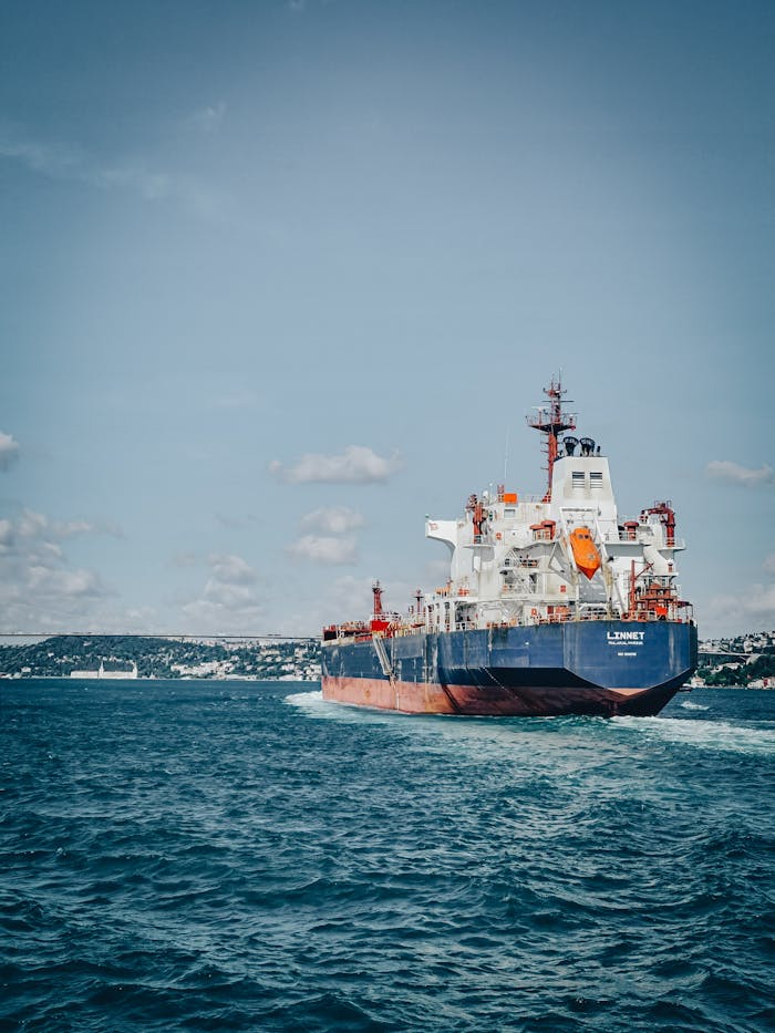 A cargo ship sails on a vast ocean under a clear sky, showcasing maritime transport.