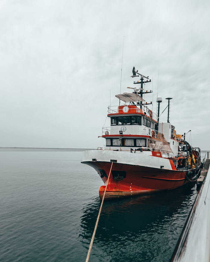 A vibrant red and white survey vessel docked at a pier under a cloudy sky, ready for maritime exploration.