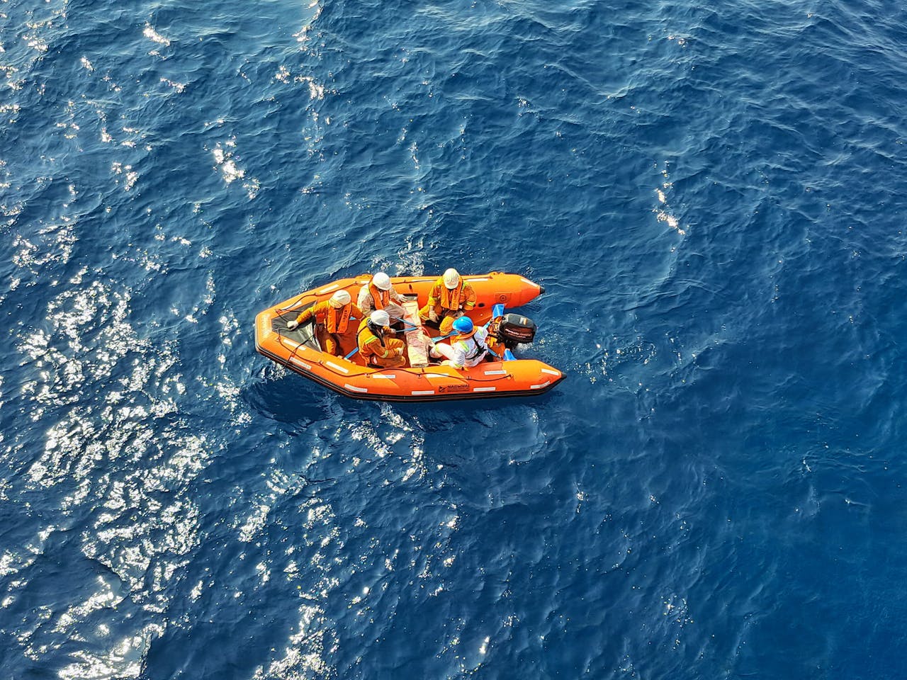 Aerial shot of an orange inflatable boat with people in safety gear navigating the open blue sea.