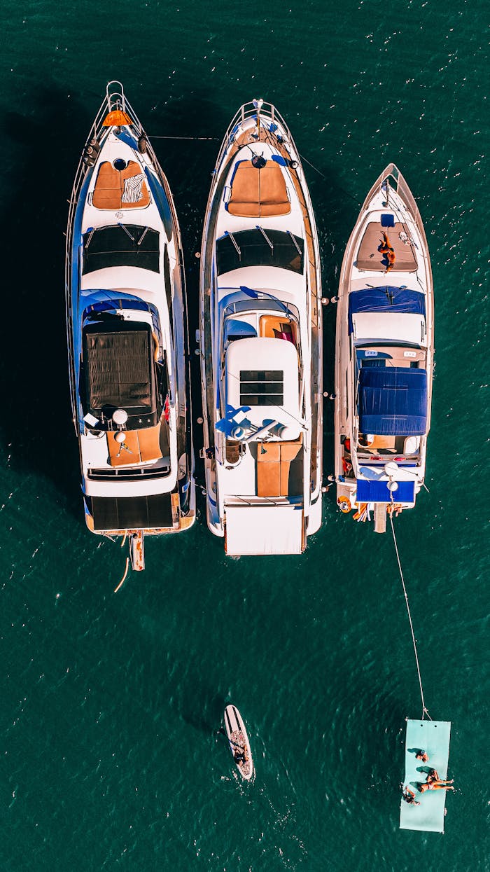 Aerial shot of three luxury yachts moored side by side in clear blue ocean, showcasing opulent leisure.