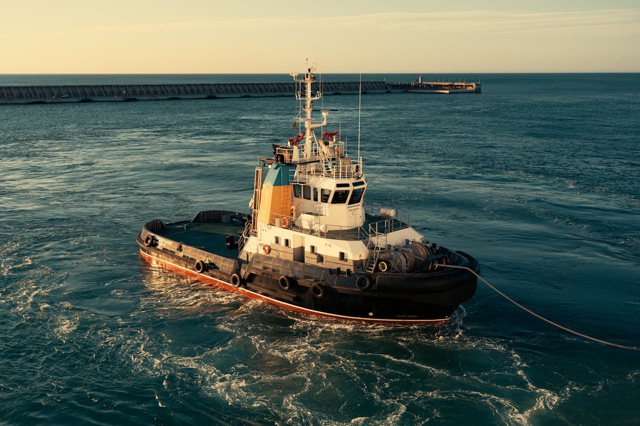 A tugboat travels through calm ocean waters at sunrise with a breakwater in the background.