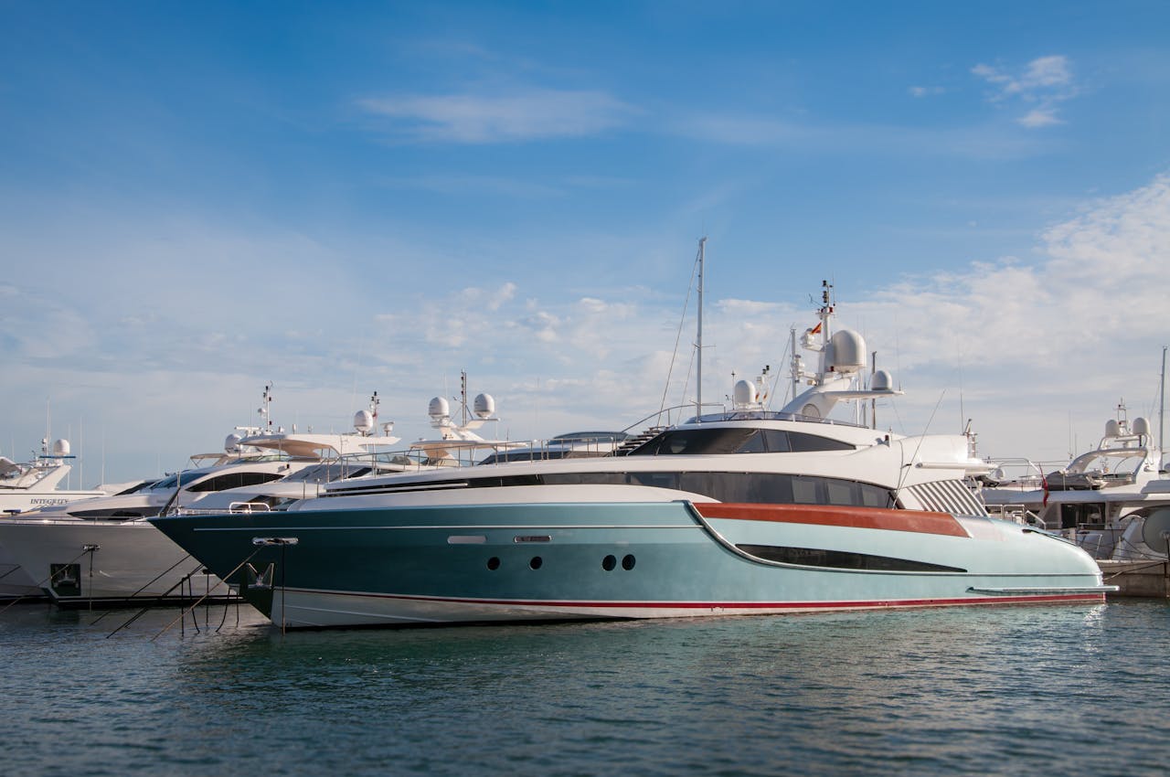 A collection of sleek yachts docked at a serene marina with a bright blue sky above.