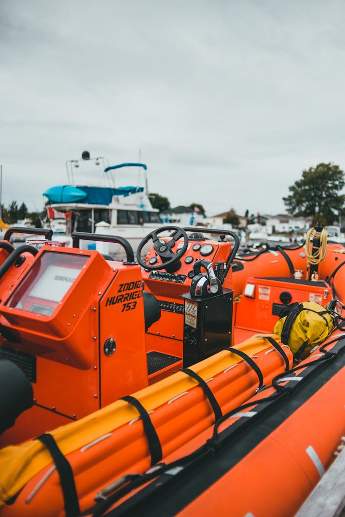 Bright orange rescue boat with marine equipment docked at a marina on a cloudy day.